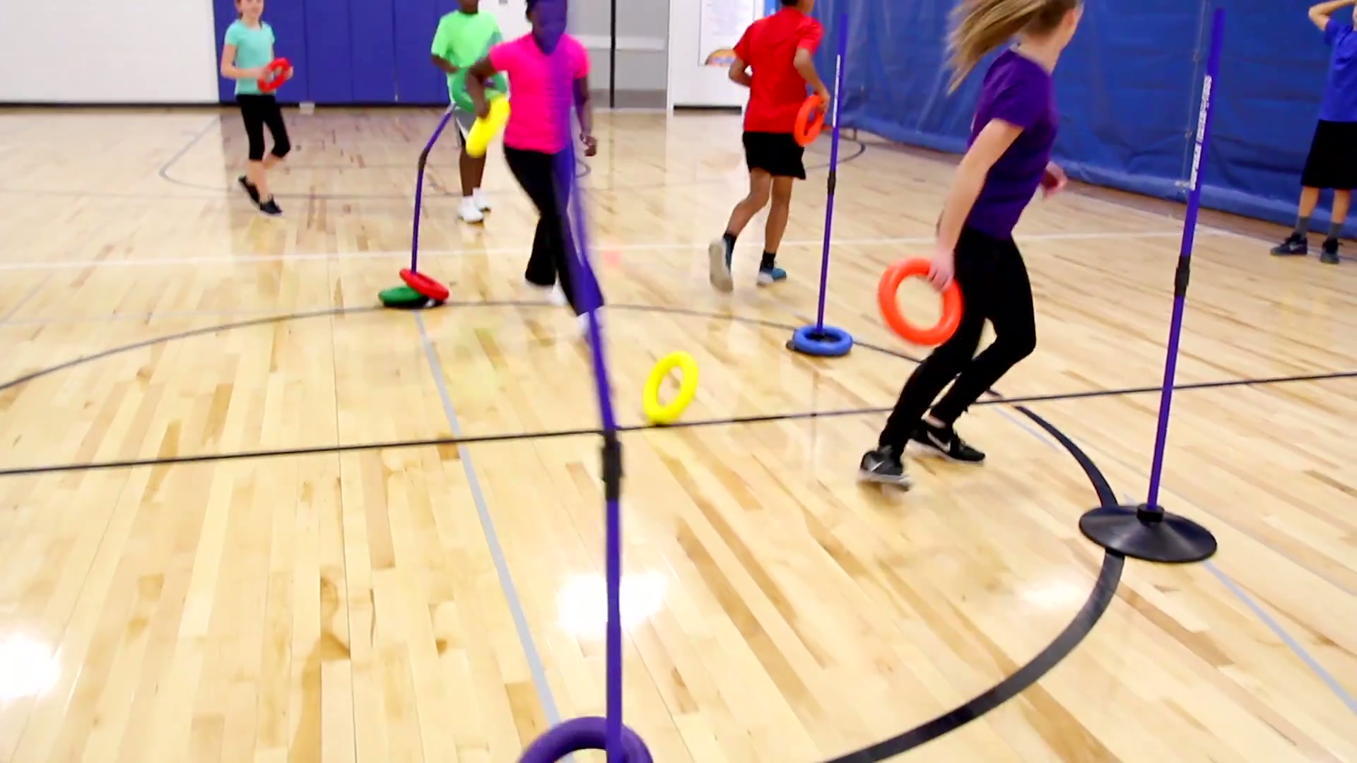 Students playing TeeterToss with poles and rings in a school gym